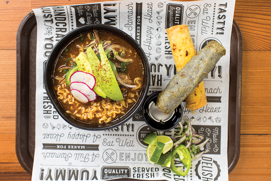 The Birria Ramen features ramen noodles, braised beef, onions, cilantro, jalepeños, raddish and avocado served with braised beef and cheese taquitos.