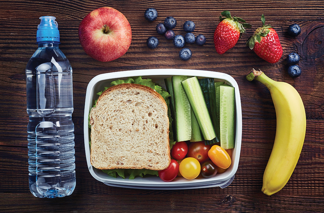 Healthy lunch box with sandwich and fresh vegetables, bottle of water and fruits on wooden background. From top view