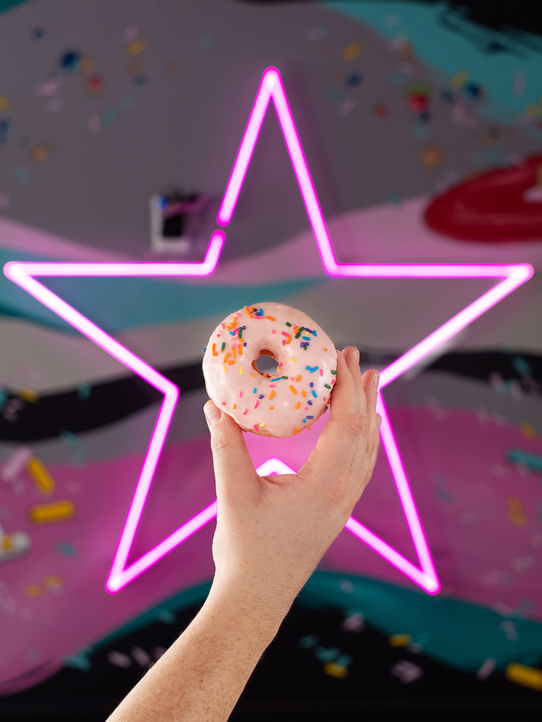 Donut held in front of the Donut Star neon sign.